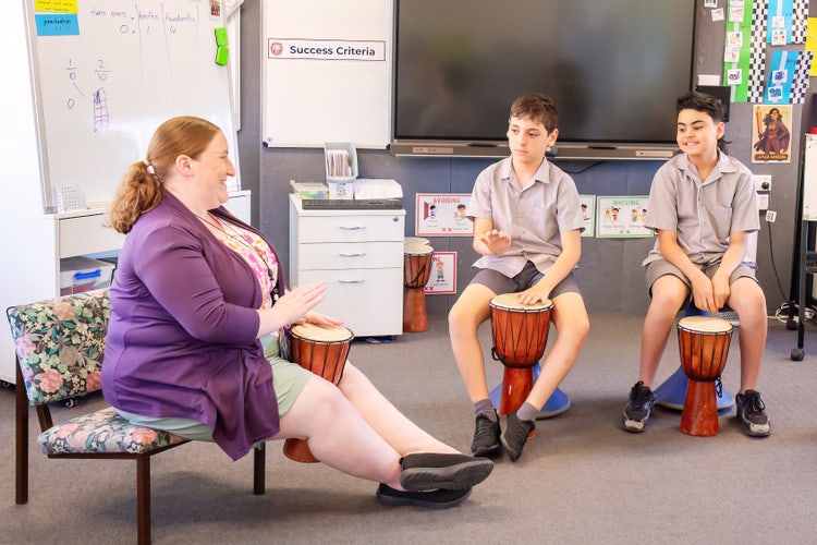 A teacher and two boys playing the drums.