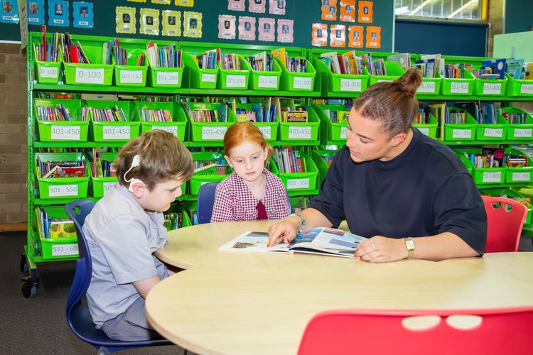 Wellbeing officer reading a book with two students.